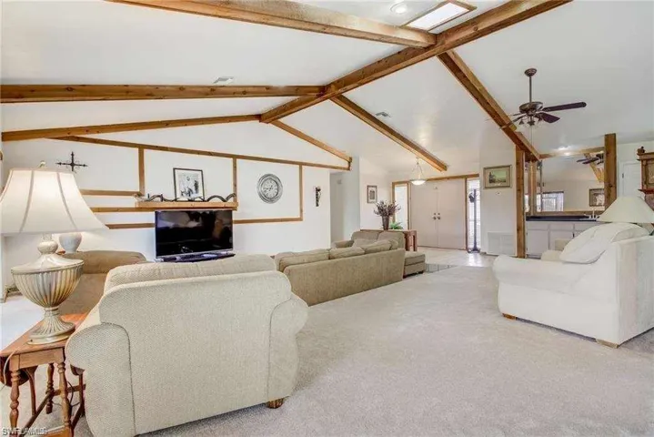 Carpeted living room featuring lofted ceiling with beams and ceiling fan