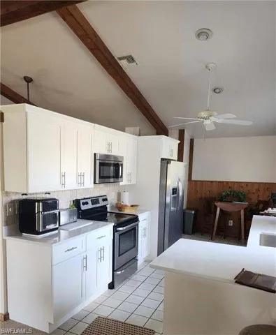 Kitchen with light tile patterned flooring, white cabinets, ceiling fan, beam ceiling, and stainless steel appliances