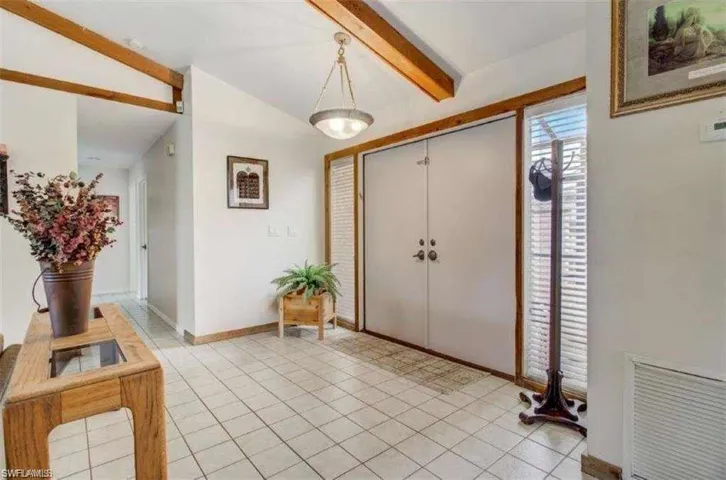 Foyer with light tile patterned floors and vaulted ceiling with beams