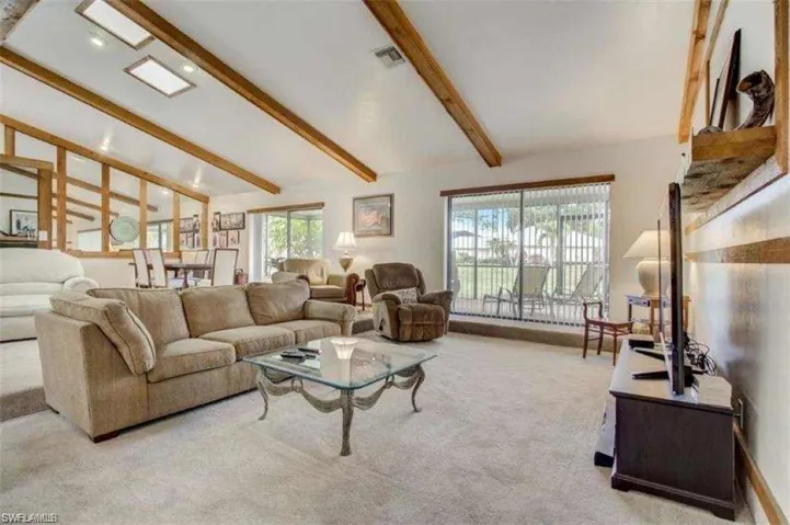Living room featuring beamed ceiling, light colored carpet, high vaulted ceiling, and a healthy amount of sunlight