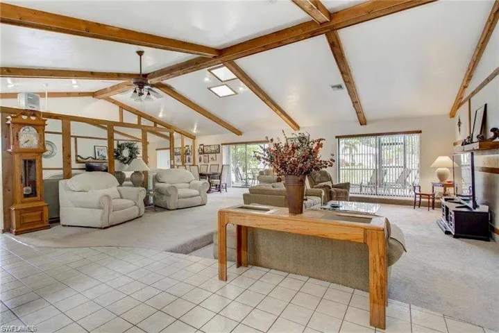 Carpeted living room featuring beam ceiling, ceiling fan, and high vaulted ceiling