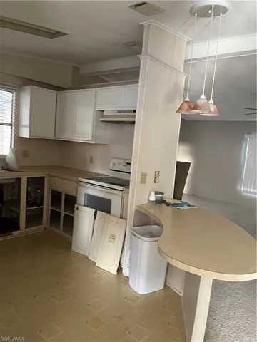 Kitchen with a peninsula, white cabinetry, crown molding, light countertops, and extractor fan