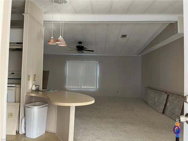 Kitchen featuring a ceiling fan, light carpet, pendant lighting, under cabinet range hood, and open floor plan