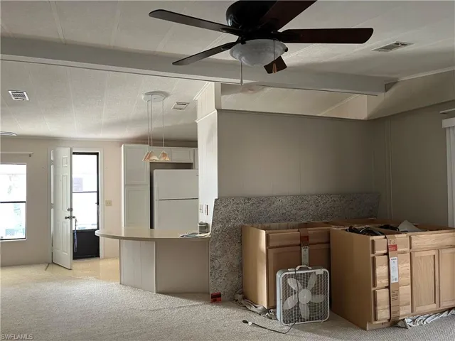Kitchen with light carpet, freestanding refrigerator, a ceiling fan, hanging light fixtures, and white cabinets
