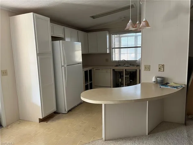 Kitchen featuring a peninsula, white appliances, lofted ceiling, pendant lighting, and light countertops