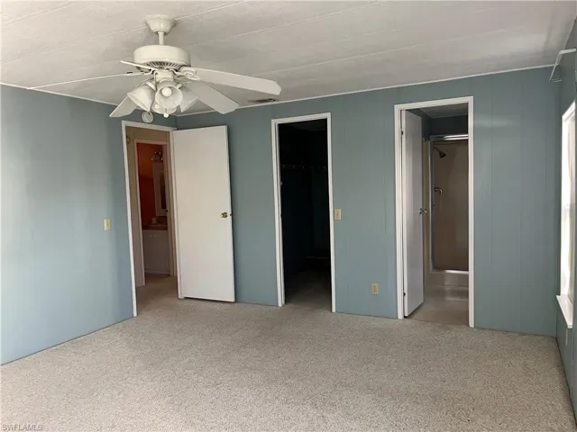 Unfurnished bedroom featuring light carpet, a walk in closet, and a ceiling fan