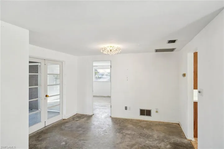 Spare room featuring a chandelier, french doors, and concrete floors