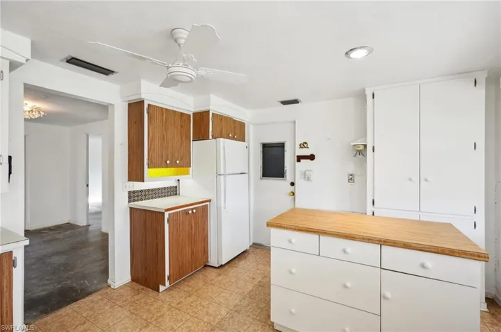 Kitchen featuring ceiling fan, white refrigerator, white cabinetry, and tasteful backsplash