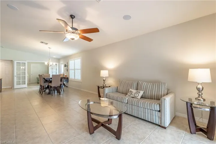 Tiled living room with ceiling fan with notable chandelier and lofted ceiling