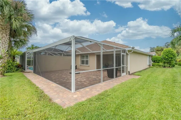 Rear view of house featuring glass enclosure, a patio area, and a lawn