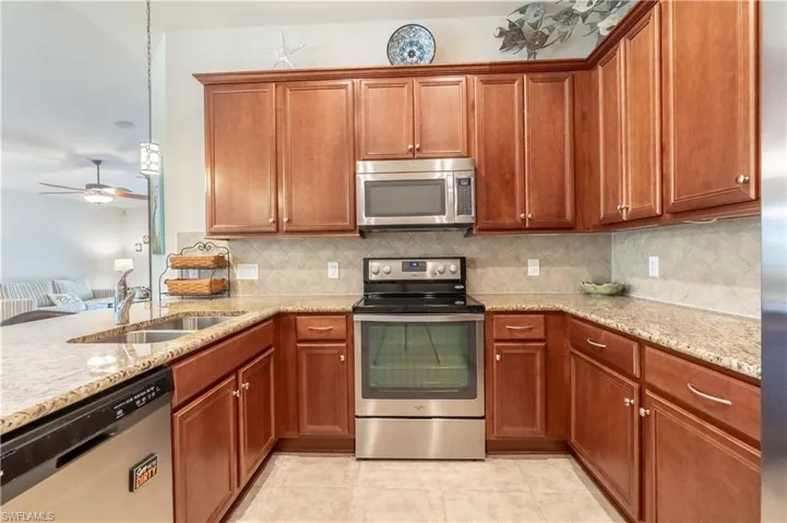 Kitchen with sink, stainless steel appliances, backsplash, light stone countertops, and ceiling fan
