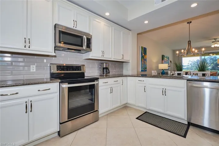 Kitchen featuring appliances with stainless steel finishes, dark stone countertops, white cabinets, recessed lighting, and hanging light fixtures