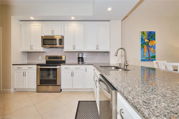 Kitchen with stainless steel appliances, dark stone counters, white cabinets, recessed lighting, and backsplash