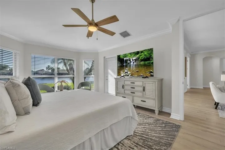 Bedroom with crown molding, light wood finished floors, arched walkways, and a ceiling fan