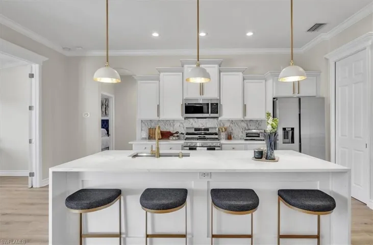 Kitchen featuring light wood-style floors, white cabinets, appliances with stainless steel finishes, light stone counters, and ornamental molding