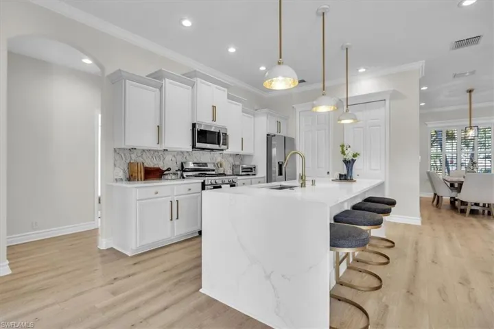 Kitchen with a breakfast bar area, white cabinets, ornamental molding, appliances with stainless steel finishes, and light stone countertops