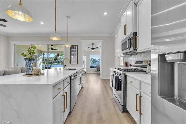 Kitchen featuring stainless steel appliances, white cabinets, light wood-style floors, open floor plan, and light stone counters