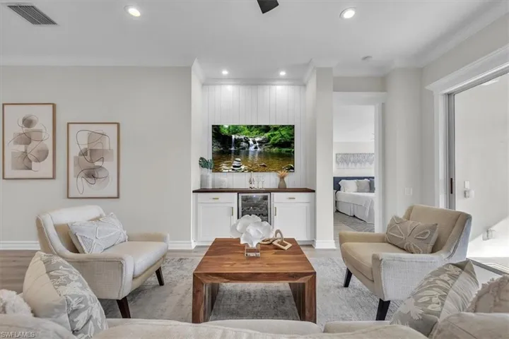 Living area with recessed lighting, ornamental molding, beverage cooler, a bar, and light wood-type flooring