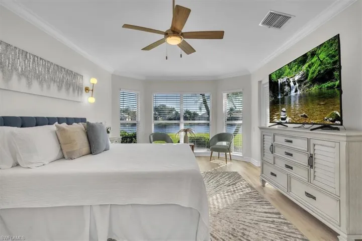 Bedroom with light wood finished floors, ceiling fan, ornamental molding, and multiple windows