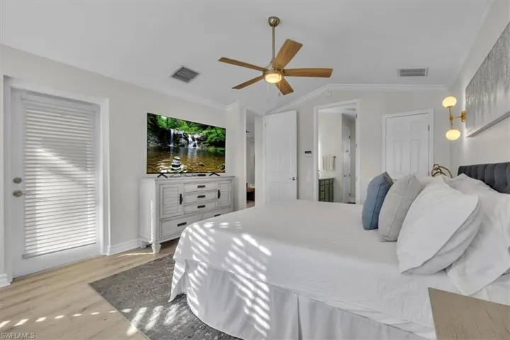 Bedroom featuring crown molding, light wood-style floors, ceiling fan, lofted ceiling, and ensuite bath