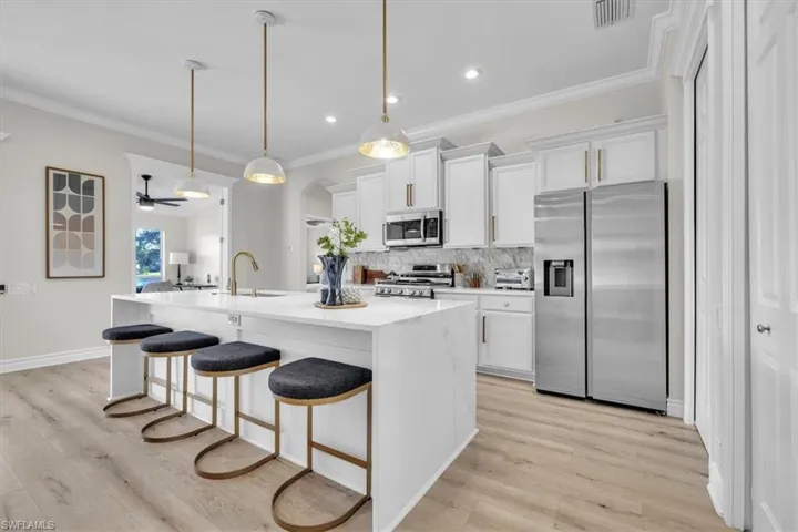 Kitchen with stainless steel appliances, white cabinets, a kitchen bar, pendant lighting, and crown molding