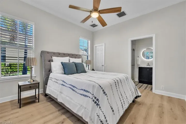 Bedroom featuring light wood-style floors, crown molding, ensuite bath, and ceiling fan