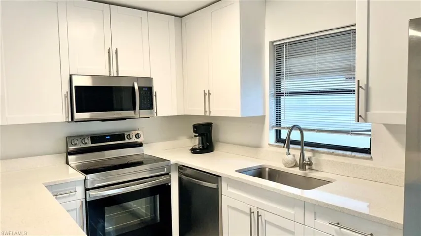 Kitchen featuring appliances with stainless steel finishes, white cabinetry, and light stone counters