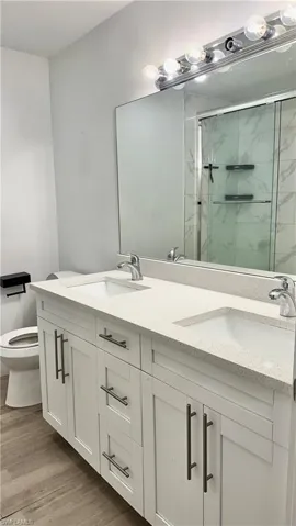 Full bathroom with double vanity, a marble finish shower, and light wood-style flooring