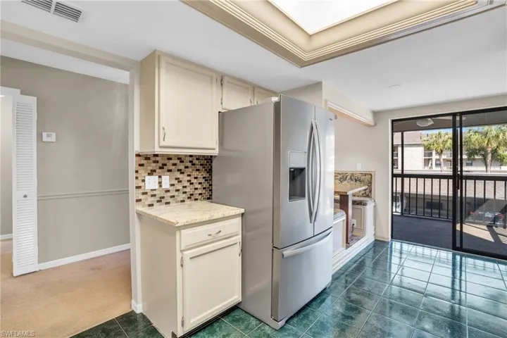 Kitchen featuring a raised ceiling, stainless steel fridge, decorative backsplash, and dark tile patterned flooring