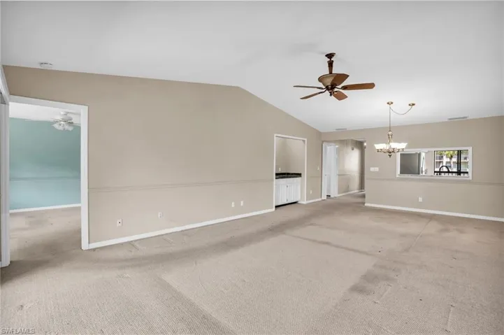 Unfurnished living room with ceiling fan with notable chandelier, light carpet, and lofted ceiling