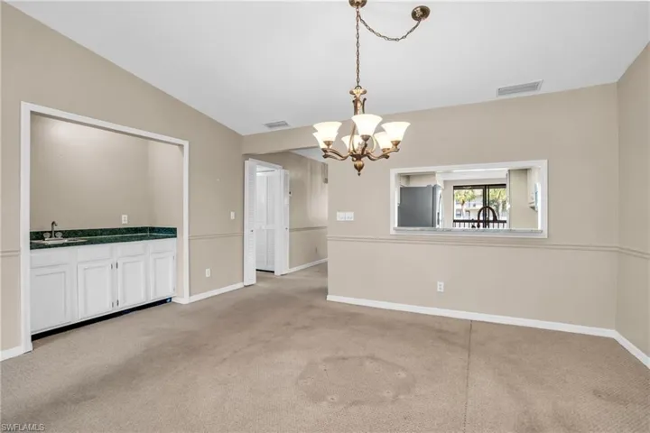 Unfurnished dining area featuring light colored carpet, sink, a chandelier, and vaulted ceiling