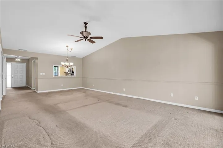 Unfurnished living room featuring ceiling fan with notable chandelier, light carpet, and vaulted ceiling