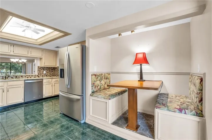 Kitchen with dark tile patterned flooring, ceiling fan with notable chandelier, appliances with stainless steel finishes, a tray ceiling, and tasteful backsplash