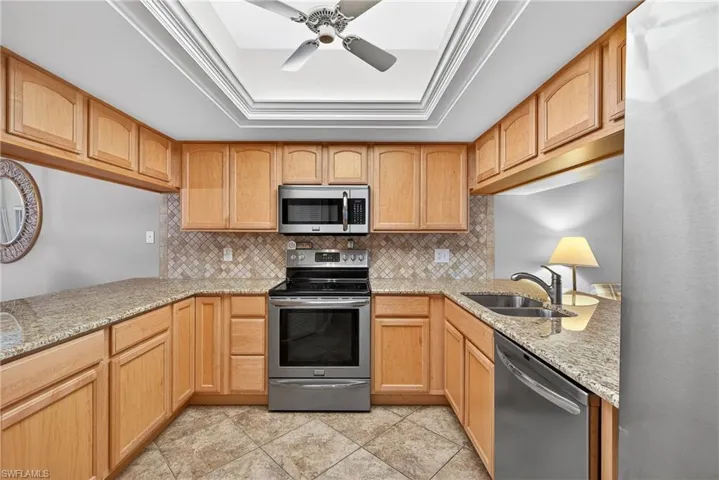 Kitchen featuring stainless steel appliances, a ceiling fan, light stone countertops, ornamental molding, and tasteful backsplash