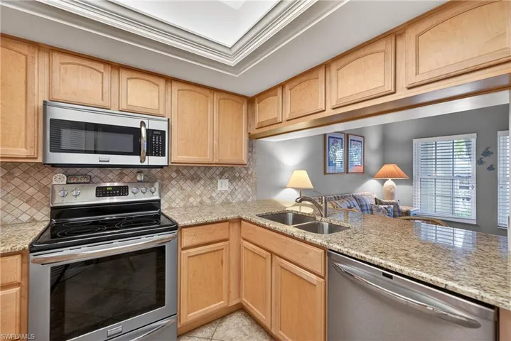Kitchen featuring stainless steel appliances, light wood finish cabinets, light stone countertops, open floor plan, and ornamental molding