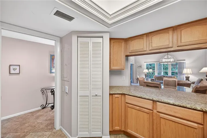 Kitchen with light wood finish cabinets, open floor plan, light stone counters, crown molding, and electric panel