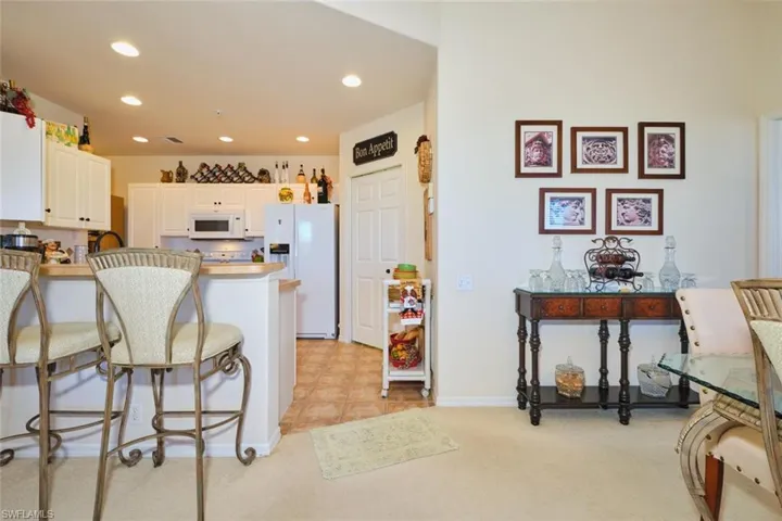 Kitchen featuring white cabinets, a breakfast bar area, white appliances, light countertops, and recessed lighting