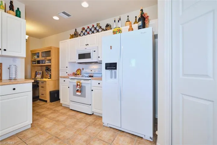 Kitchen with white appliances, light countertops, white cabinets, light tile patterned floors, and recessed lighting