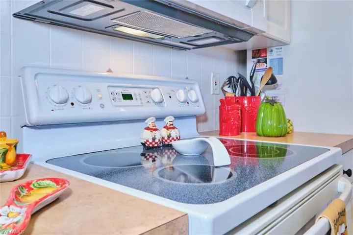 Kitchen view of white range with electric stovetop, range hood, white cabinetry, and tasteful backsplash