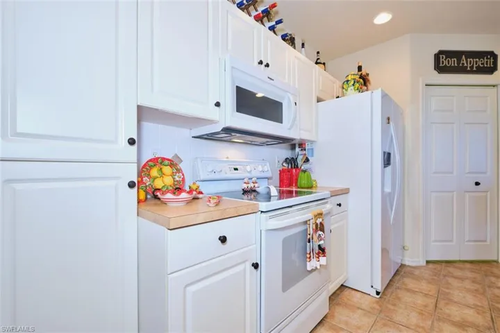 Kitchen with white appliances, white cabinets, light countertops, light tile patterned flooring, and recessed lighting