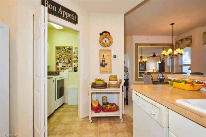 Kitchen with dishwasher, light countertops, hanging lights, washing machine and dryer, and white cabinetry
