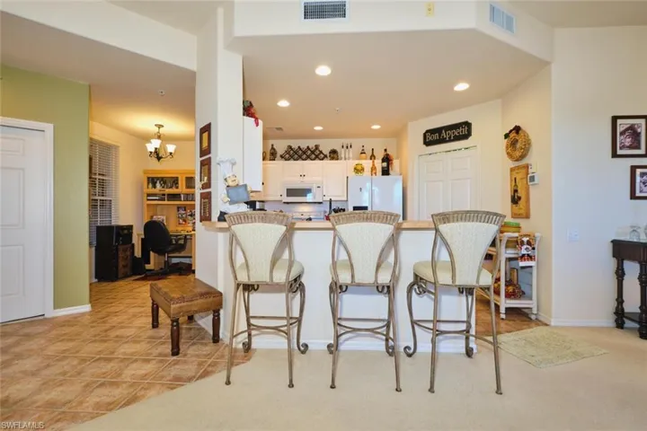 Kitchen with a breakfast bar, a peninsula, white cabinetry, white appliances, and suspended lighting