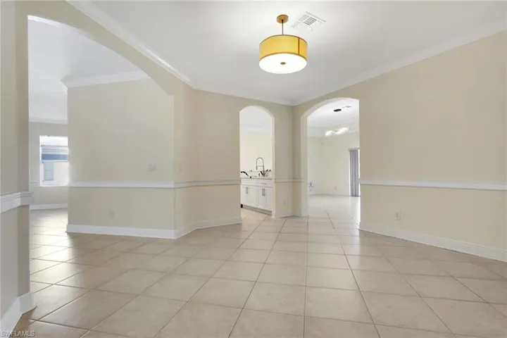 Unfurnished room featuring arched walkways, ornamental molding, and light tile patterned floors