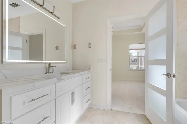 Bathroom with vanity, light colored carpet, light tile patterned flooring, crown molding, and a tub to relax in