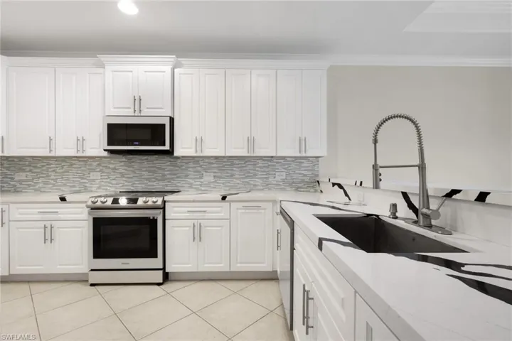 Kitchen featuring stainless steel appliances, white cabinets, light stone countertops, decorative backsplash, and ornamental molding