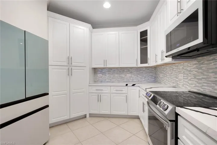 Kitchen featuring electric stove, freestanding refrigerator, white cabinets, glass insert cabinets, and light tile patterned floors
