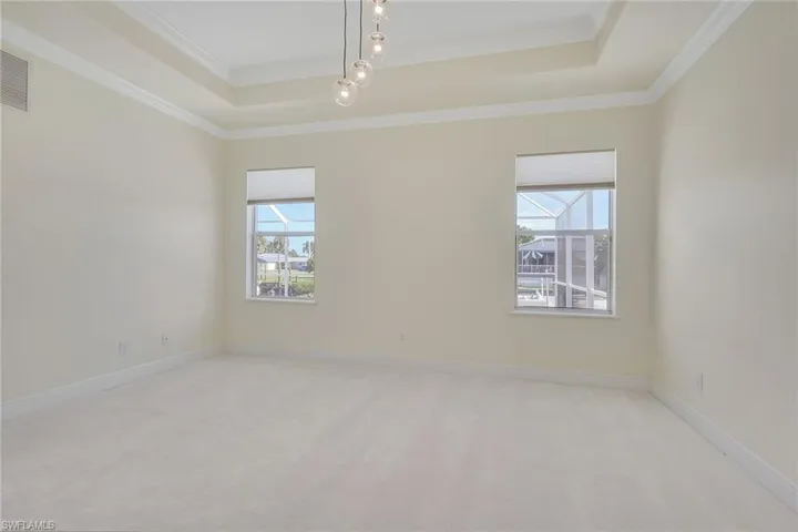 Spare room featuring a raised ceiling, crown molding, and light carpet