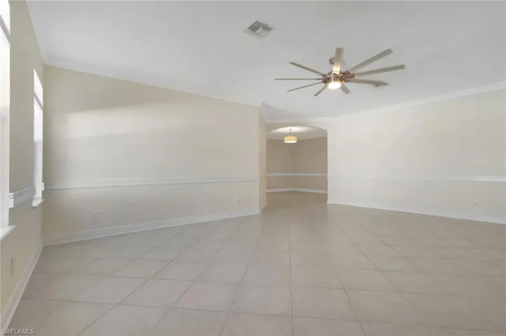 Unfurnished room featuring arched walkways, crown molding, a ceiling fan, and light tile patterned floors
