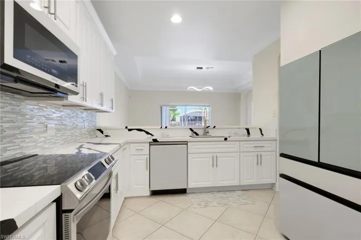 Kitchen featuring stainless steel appliances, white cabinetry, light countertops, ornamental molding, and recessed lighting