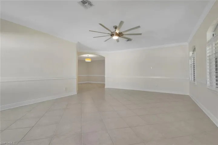 Unfurnished room with arched walkways, ornamental molding, a ceiling fan, and light tile patterned flooring